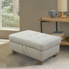 a white ottoman sitting on top of a carpeted floor in front of a window