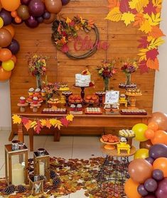 an autumn themed dessert table with fall leaves on the floor and balloons in the air