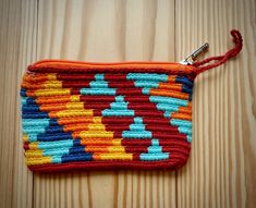 an orange, blue and yellow crochet purse on a wooden surface with a metal hook