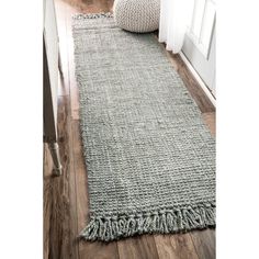 a gray rug with fringes on the floor in front of a white door and window