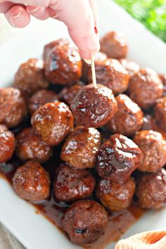 someone is picking up some meatballs from the plate with sauce on them and holding a toothpick in their mouth