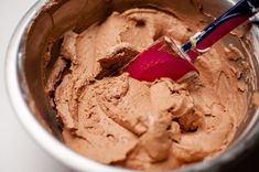 a red spatula in a metal bowl filled with chocolate frosting