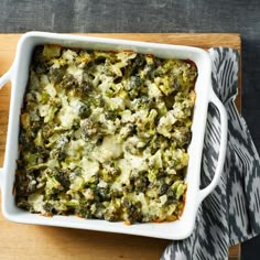 a casserole dish with broccoli and cheese in it on a wooden cutting board