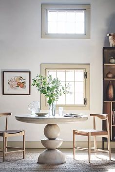 a dining room table with chairs and vases on it in front of a window