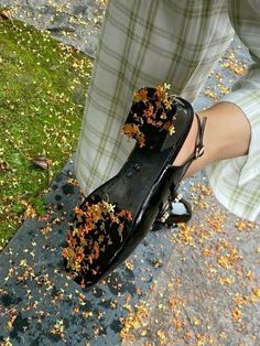 a person wearing black shoes with fall leaves on the bottom of their shoelaces