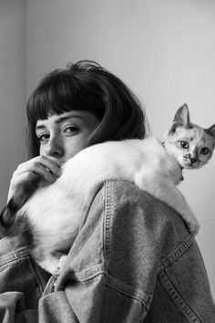 a woman holding a cat in her arms and looking at the camera while wearing a denim jacket