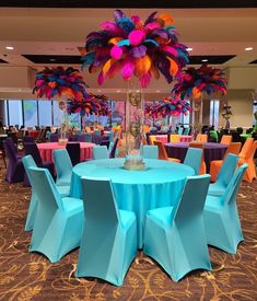 a blue table topped with lots of colorful chairs next to a tall vase filled with feathers