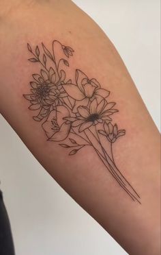 a black and white photo of some flowers on a woman's arm with tattoos