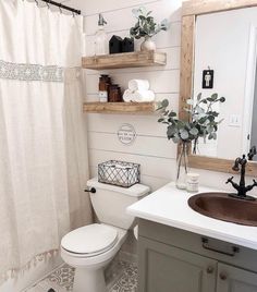 a white toilet sitting next to a bathroom sink under a mirror on top of a wooden shelf