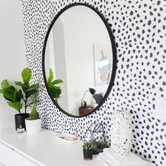 a white dresser topped with a mirror next to a wall covered in black and white polka dots