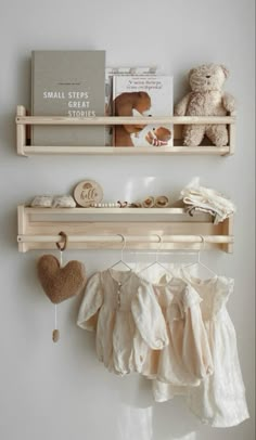 two wooden shelves with clothes hanging from them and a teddy bear on the shelf next to it