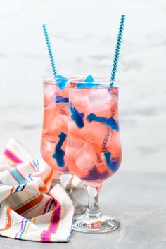 two glasses filled with pink and blue liquid sitting on top of a table next to a napkin