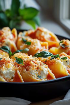 pasta shells with sauce and cheese in a black dish on a table next to a window