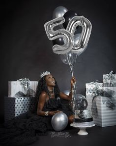 a woman sitting on the ground with balloons and presents in front of her, wearing a tiara