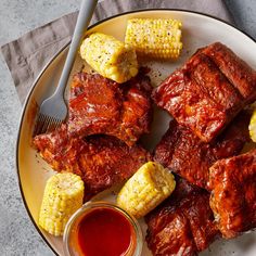 a plate with ribs and corn on the cob next to ketchup sauce