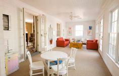 a living room filled with furniture and a white table surrounded by red couches in front of a window