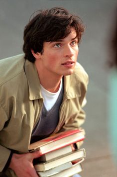 the young man is holding several books in his hands and looking at something with an amazed look on his face