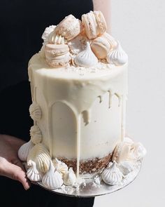 a person holding a cake with white icing and shells on the top, in front of an instagram post