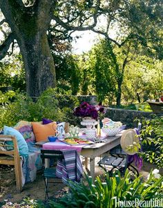 an outdoor dining area with table, chairs and colorful pillows on the bench in front of trees