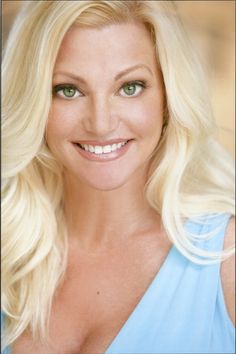 a woman with long blonde hair and green eyes smiling at the camera while wearing a blue dress