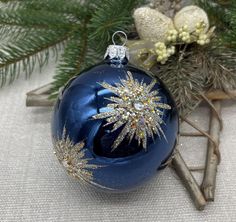 a blue christmas ornament sitting on top of a table next to evergreen branches