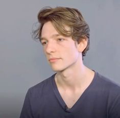 a young man with brown hair wearing a v - neck shirt and looking at the camera