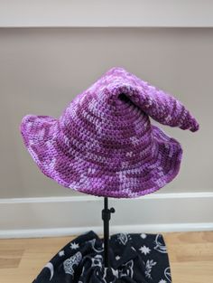 A handmade crochet witch hat made with purple mottled acrylic yarn. Made to be slouchy and comfy, with a moldable wire brim. Cozy muted purples ranging from lavender to deep eggplant.  Hat has a 11" diameter straight across the brim at the widest point. The inside circumference is roughly 20-22" - it can stretch a bit. Pattern: TheEntangledFae - https://www.etsy.com/shop/TheEntangledFae Handmade Witchy Hat With Curved Brim, Adjustable Purple Halloween Hat, Purple Adjustable Crochet Hat, Purple Bohemian Brimmed Hat, Purple Crochet Bohemian Hat, Purple Hat With Curved Brim One Size Fits Most, Purple Yarn Cap, Purple Hand Knitted Brimmed Hat, Purple Halloween Costume Hat