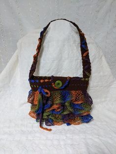 "Fancy hand crocheted handbag or shoulder bag. Crocheted in deep brown acrylic yarn, nice a tight stitch (no holes for bits to fall out!). This is a medium size, shoulder bag style handbag or purse. There is a glittering ruffled fancy yarn in shades of green, orange, brown and blue crocheted in all around. Trimmed all along the shoulder strap as well. Folder over flap with a large button for keeping the bag closed and secure. A fun and flirty look for any occasion. Medium length shoulder strap. Brown Crochet Bag For Gift, Brown Crochet Bag Gift, Brown Crochet Shoulder Bag Gift, Crochet Brown Shoulder Bag Gift, Brown Crochet Shoulder Bag As Gift, Brown Crochet Shoulder Bag For Gift, Crochet Brown Shoulder Bag For Gift, Brown Rectangular Crochet Bag For Party, Brown Yarn Crochet Bag