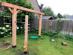 a wooden swing set in the middle of a yard with green grass and plants around it