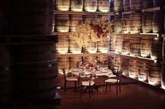 a room filled with lots of barrels and tables covered in white tablecloths next to wine glasses