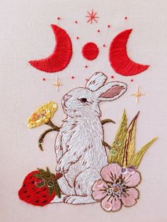 a white rabbit sitting on top of a table next to a red moon and strawberry