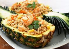 two pineapple halves with rice and shrimp in them on a white plate next to a green leaf