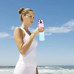 a woman standing on the beach holding a water bottle