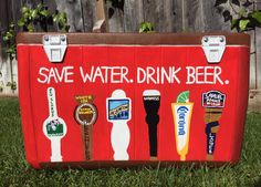 a cooler with some beer on it sitting in the grass next to a wooden fence