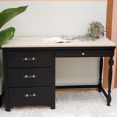 a black desk with three drawers and a potted plant next to it on a white rug