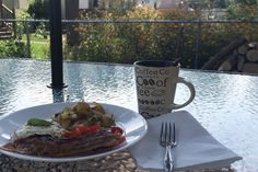 a white plate topped with meat and vegetables next to a coffee cup on top of a table