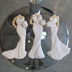 three decorated cookies in the shape of brides on a glass plate next to a candle