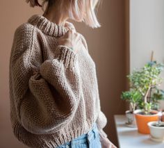 a woman standing in front of a window wearing a sweater