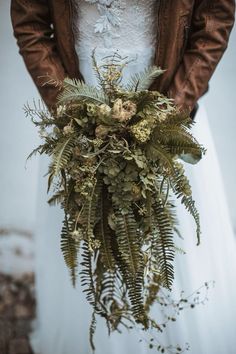 a woman in a white dress holding a bouquet of ferns and other greenery on her wedding day