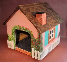 a toy house with a dog in the door and a fence around it on a pink background