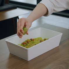 a person scooping guacamole into a white container