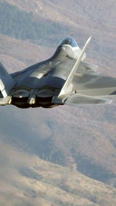 a fighter jet flying through the air with mountains in the background