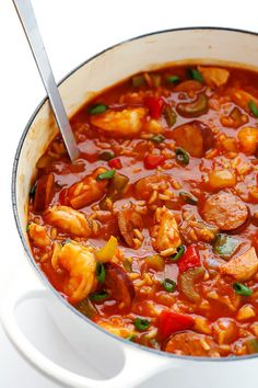 a large pot filled with lots of food on top of a white table next to a silver spoon