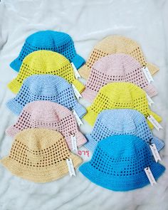 six crocheted hats with price tags are laid out on a white sheet,