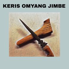 a pair of scissors sitting on top of a piece of wood with the words keris omyang jumbe