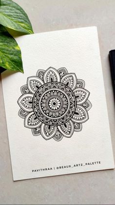 a card with an intricate design on it next to a pen and some green leaves