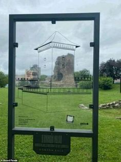 the reflection of an old castle in a glass display case on green grass with trees and buildings behind it