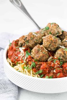 a white bowl filled with spaghetti and meatballs covered in marinara sauce next to a fork