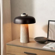 a table lamp sitting on top of a wooden dresser next to a bowl and framed photograph