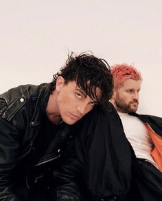 two young men are sitting next to each other, one is wearing a leather jacket